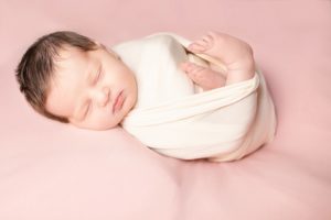 Newborn girl in cream wrap with pink blanket