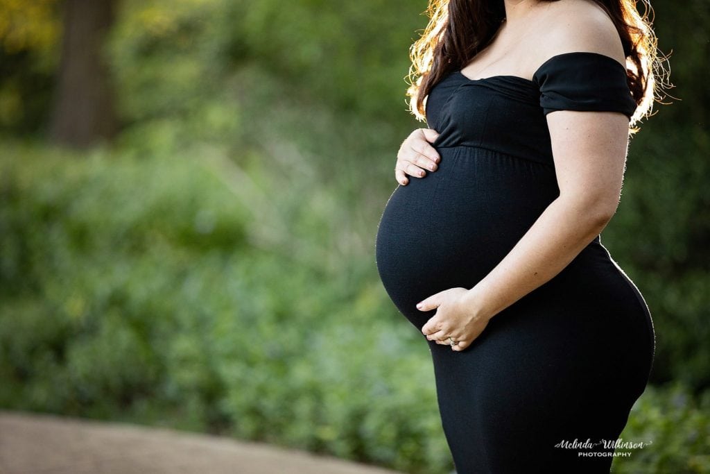 pregnant woman in a black dress in a park for a maternity session