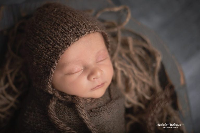 Newborn boy in brown wrap with bonnet