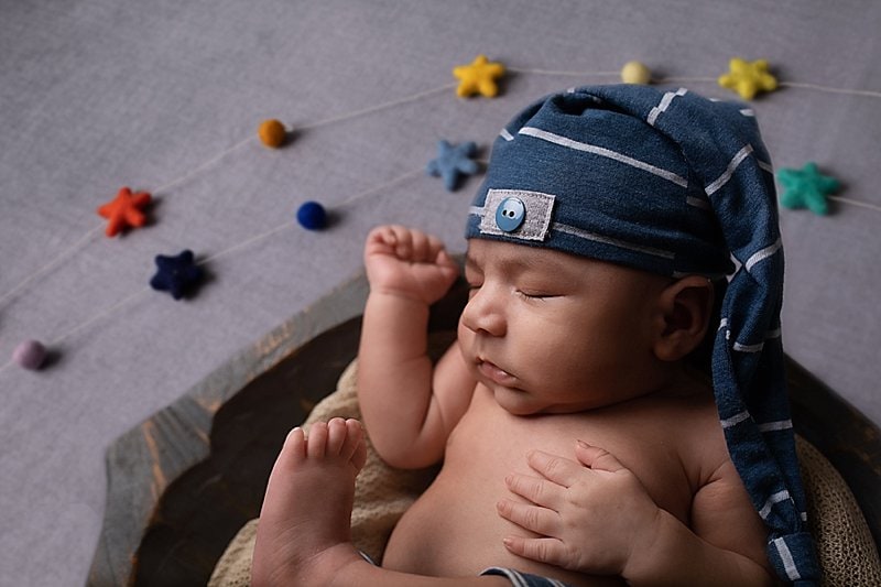 Baby boy with blue striped hat in a bowl with felted rainbow stars in background