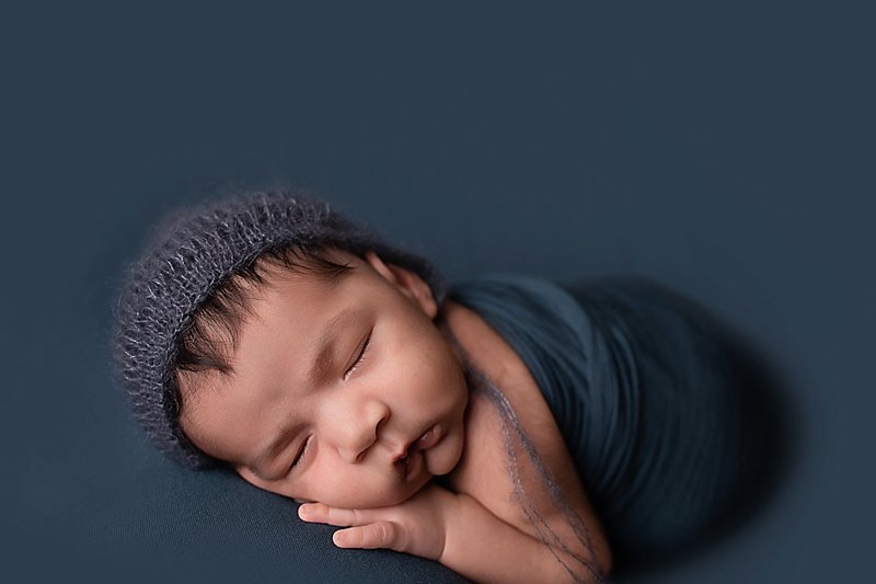 Newborn boy on blue with blue wrap and a blue knitted hat