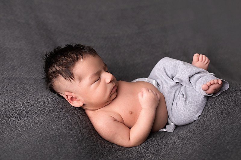 Newborn boy with gray pants on a gray blanket