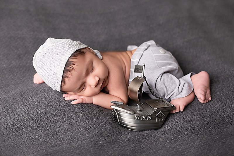 Newborn boy with gray pants and sleepy hat on a gray blanket