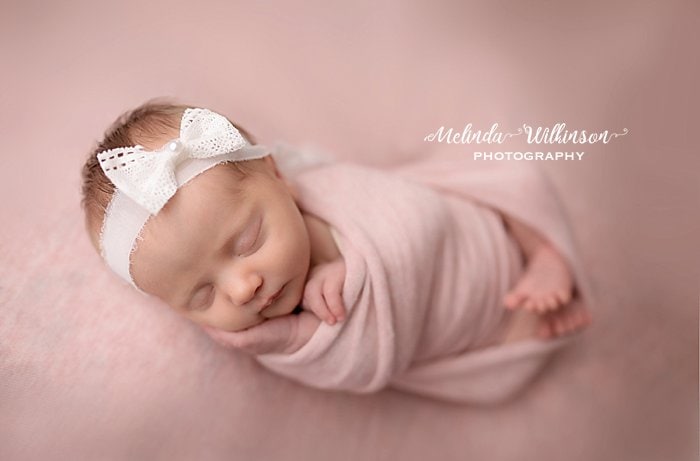 newborn girl wrapped in pink with white bow