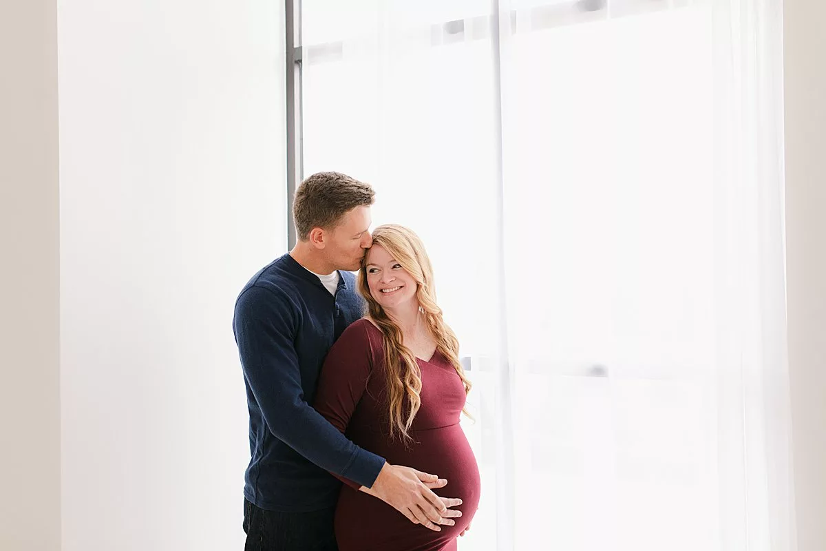 Indoor studio maternity session with big window and burgundy maternity gown