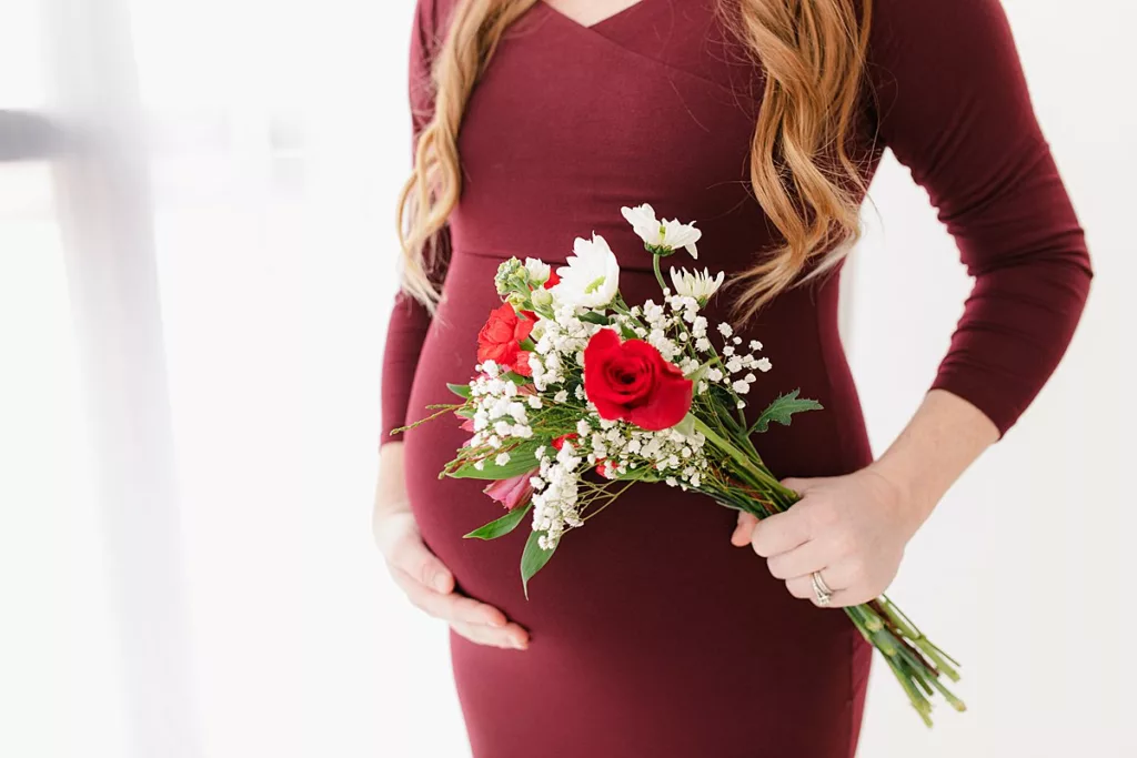 maternity pictures with burgundy gown and red and white flowers