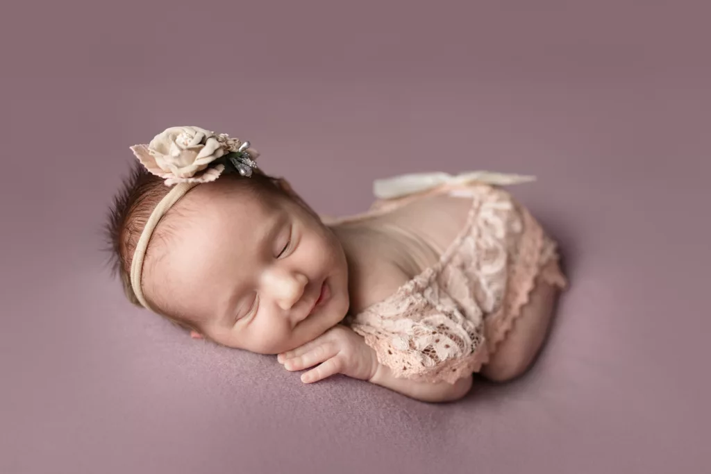 Newborn girl in a pink lacy outfit with a bow on a purple blanket