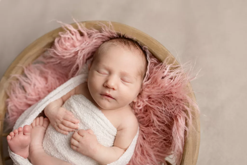Newborn girl in a white wrap on a pink fur blanket