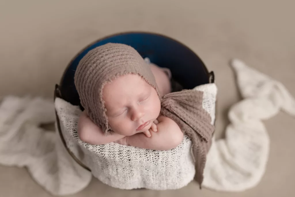 Newborn boy with brown bonnet in a blue bucket