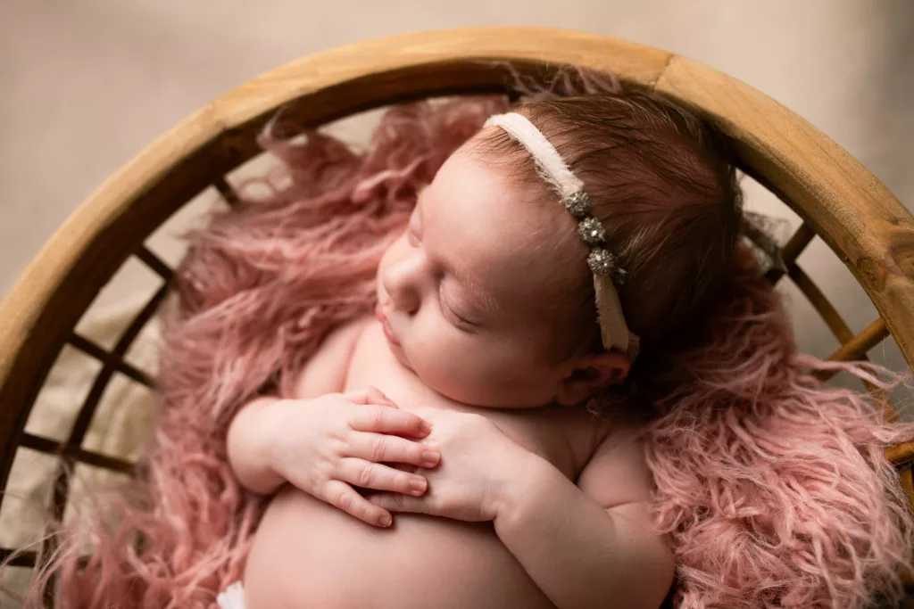 Newborn baby girl in a wooden bowl with pink fur and a headband