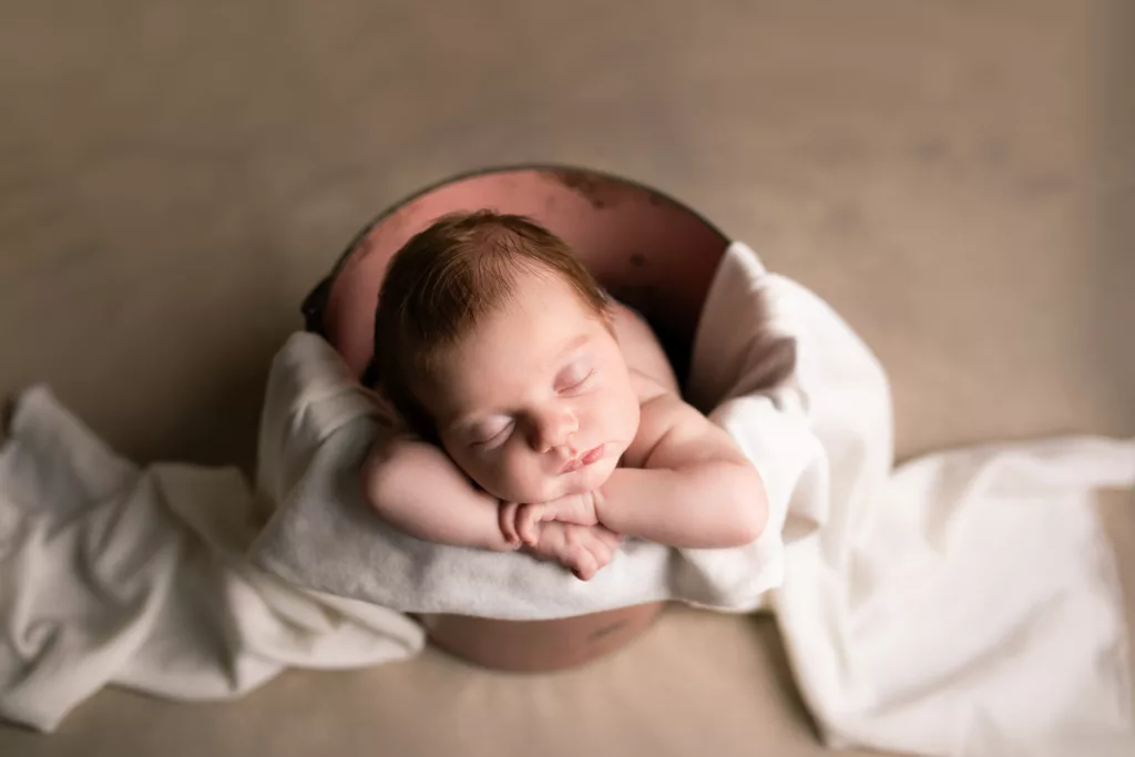 Newborn baby girl in a pink bucket with a white blanket