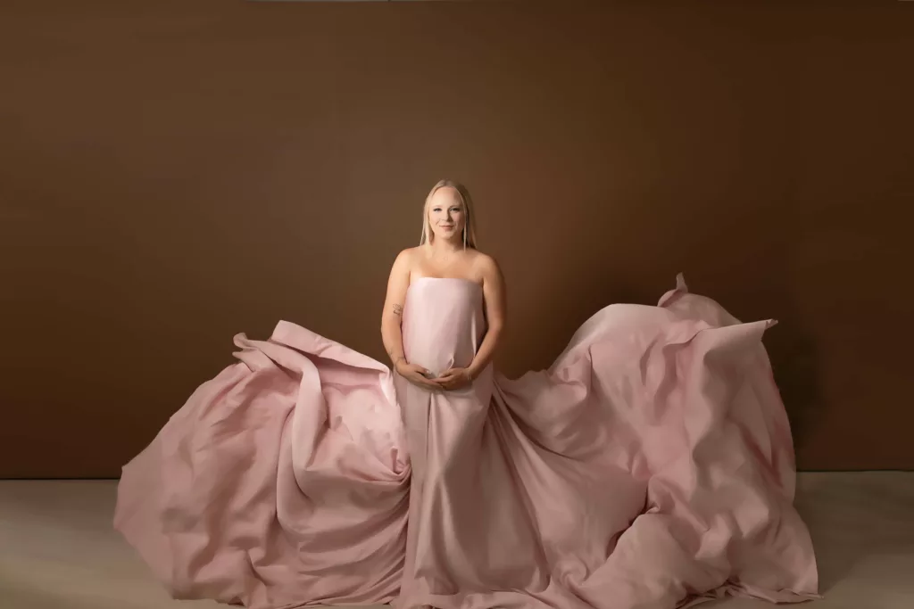 Pink maternity gown with large train in studio on brown backdrop