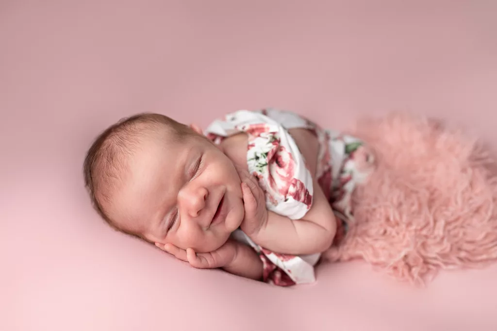 newborn girl smiling in floral outfit on pink blanket