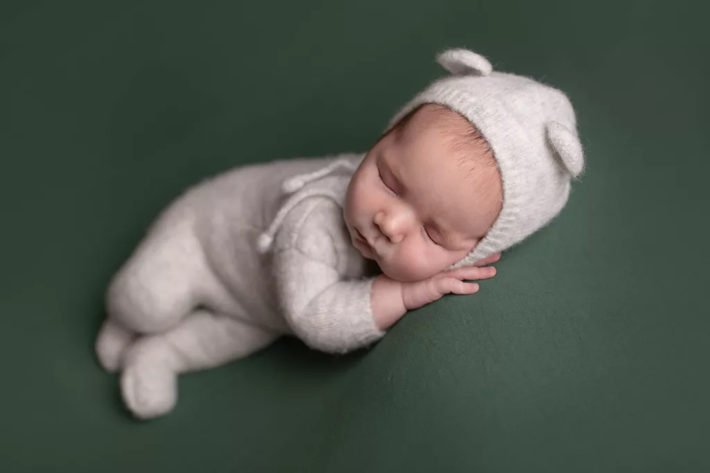 newborn boy on green blanket in gray bear knit outfit