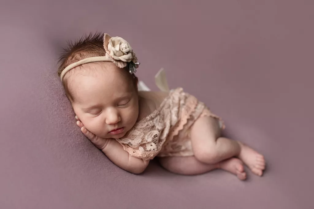 newborn girl with bow and lacy outfit on purple blanket